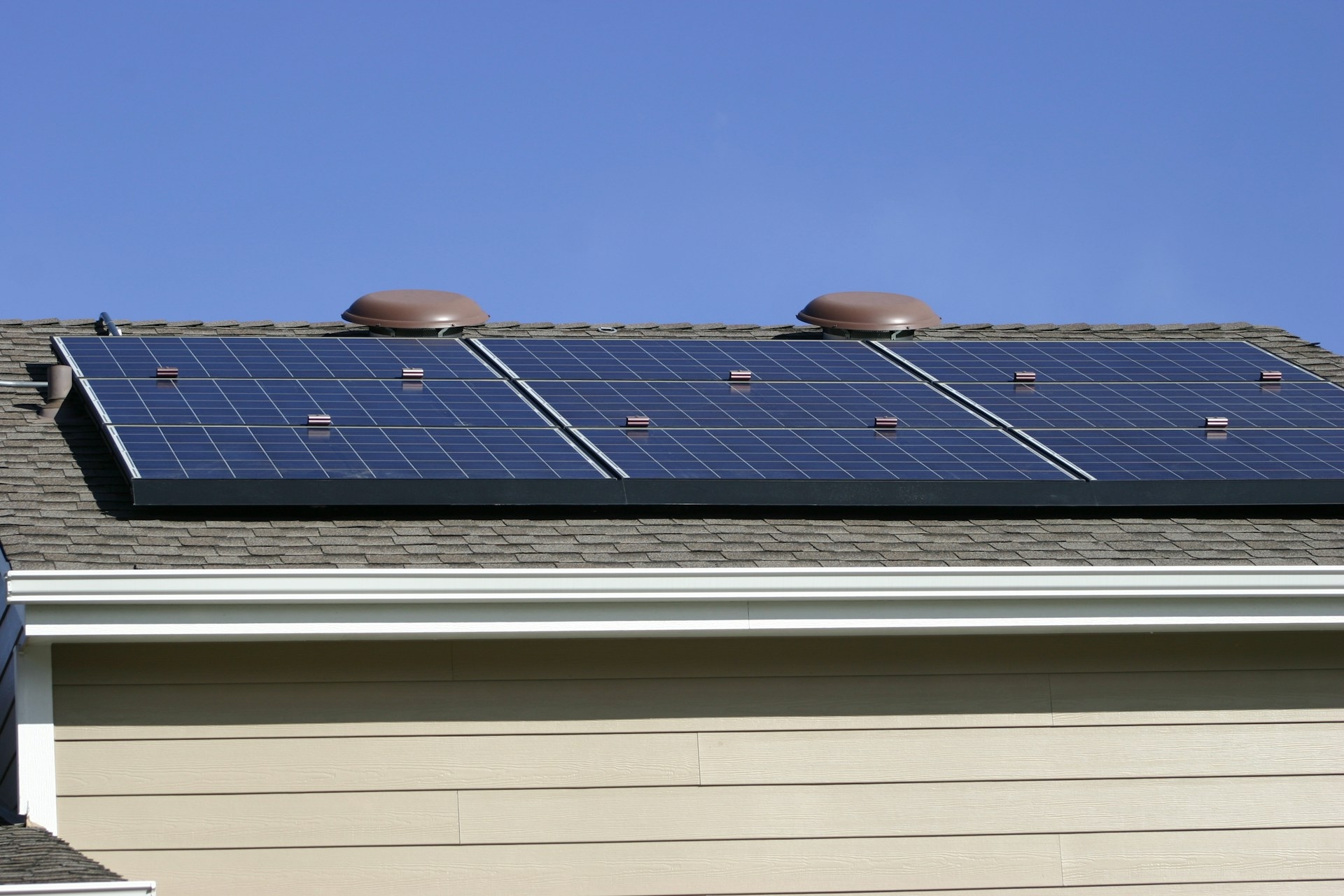 Three side-by-side solar panels on the grey roof of a tan home