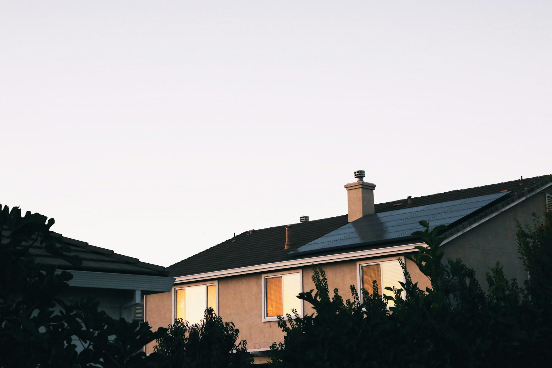 Three side-by-side solar panels on the grey roof of a tan home